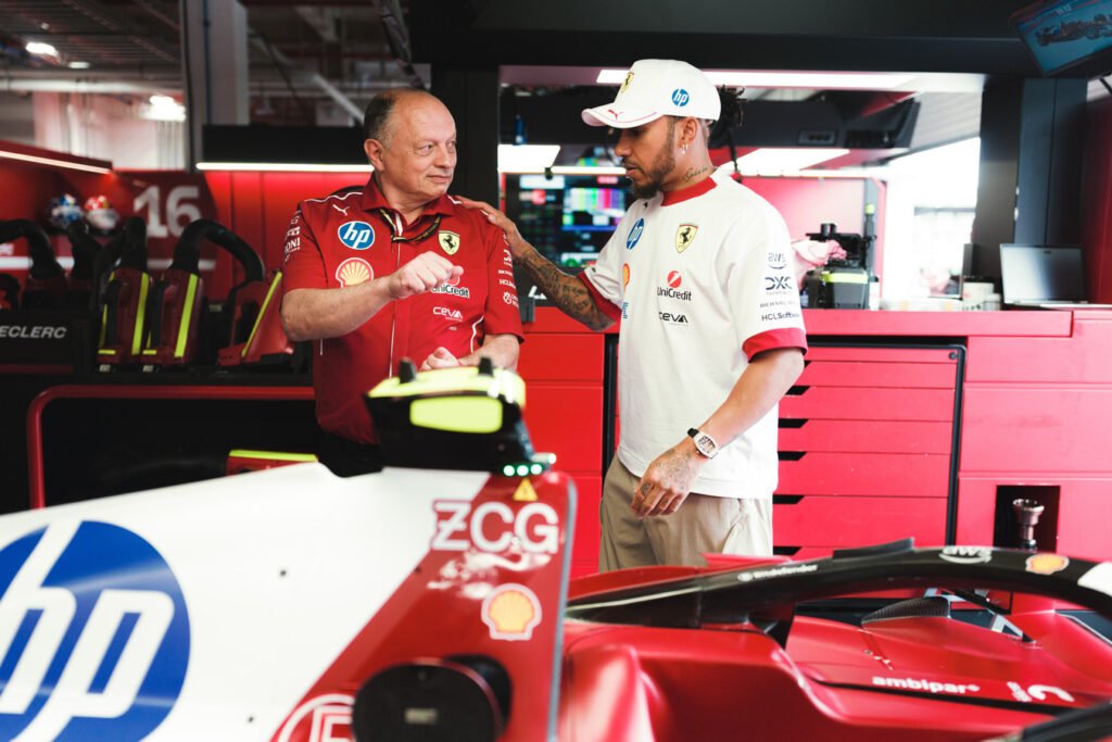 Lewis Hamilton and Fred Vasseur talk in the paddock while standing next to Hamilton's Ferrari F1 Car